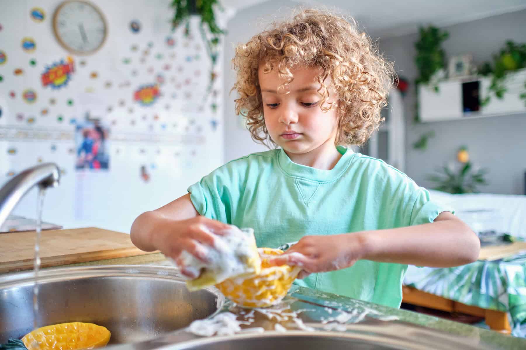 a child standing at a kitchen sink washing dishes