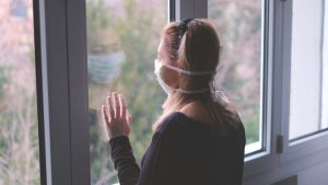Woman looking out the window wearing a medical mask