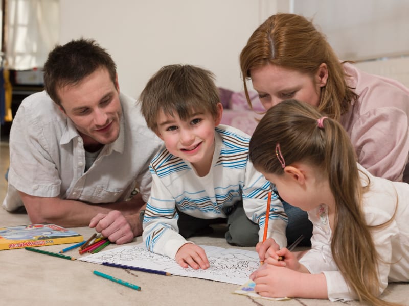 Boy Coloring Pictures While Family Looking At It On Floor